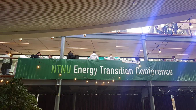 Above a large banner reading "NTNU Energy Transition Conference", the backs of people with Scientist Rebellion lab coats can be seen.