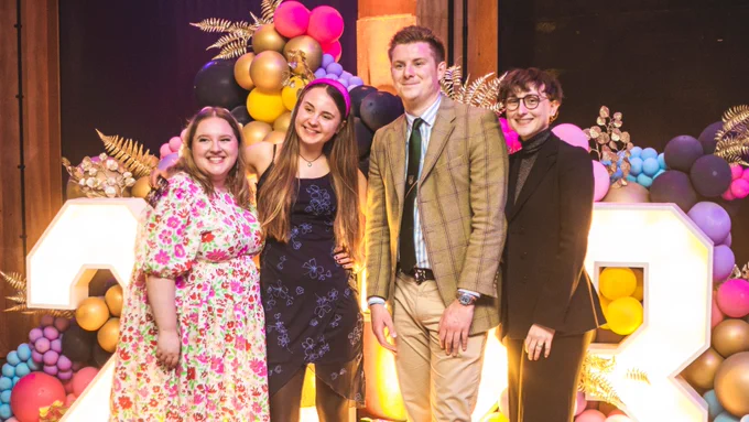 Izzie, Emma, Jack and Lily (2022/23 Full-Time Officers for the Students' Guild) are posing together in front of a large display of light-up numbers and colourful balloons.
