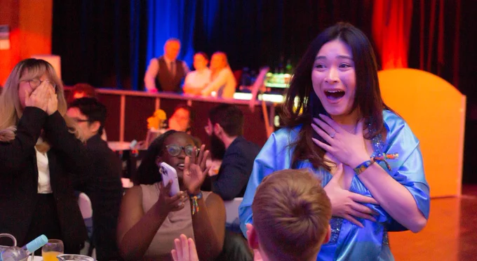 A student has her hands on her chest as she feels overwhelming excitement for winning an awards. The students around her are happy and clapping.