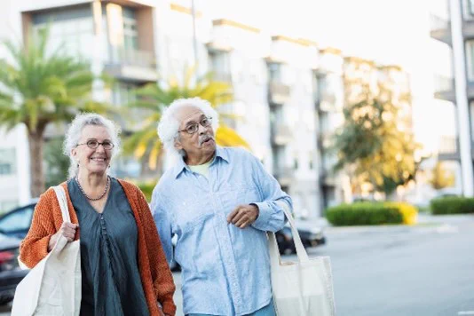 An older couple, out walking and carrying large tote bags. 