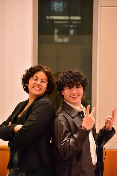 Corinne Floyd with arms crossed and Danny Islas Becker holding peace signs, both standing back to back, smiling at the camera. Photo by Marty Hightower.