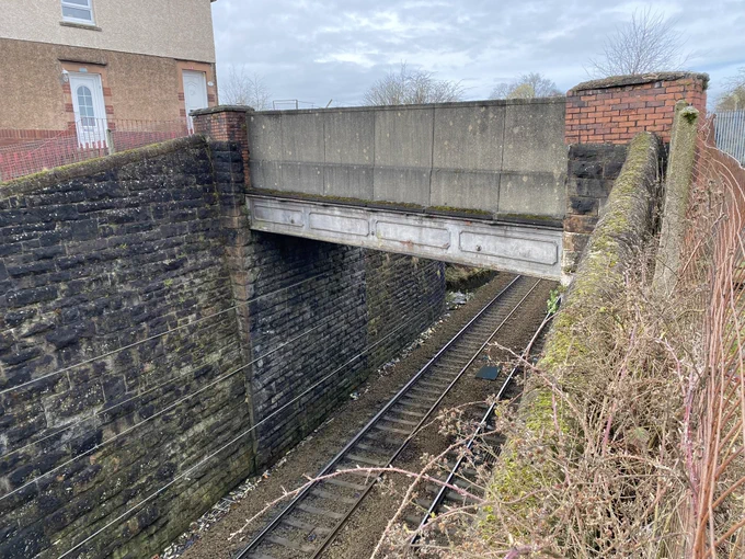 A LANDSCAPE FORMAT COLOUR PHOTOGRAPH OF A RAILWAY LINE IN A STONE-LINED CUTTING. A FLAT BRIDGE CROSSES THE CUTTING. IT HAS CONCRETE PARAPETS SUPPORTED BY BIG IRON BEAMS.