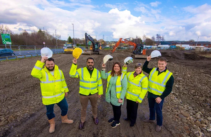 Image shows group raising hard hats on a building site