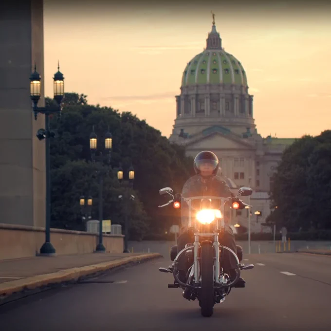 Someone riding a motorcycle with the PA State Capitol building behind them