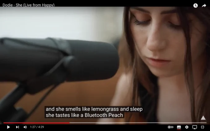 A screenshot from dodie singing 'she' the captions state the lyrics are 'she tastes like a Bluetooth Peach'  