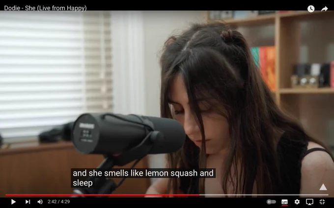 A screenshot from dodie singing 'she' the captions state the lyrics are 'and she smells like lemon squash and sleep' 