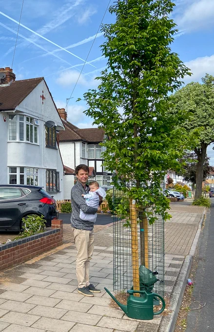 Philippe hold his baby child next to the tree he's sponsored out in his street.