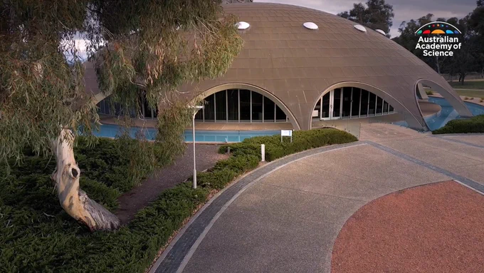 A domes building is shown with archways around the perimeter. A gumtree is in the foreground. 