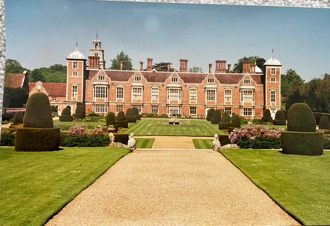 View of Jacobean brick hall with formal gardens in front and gravel path leading towards it
