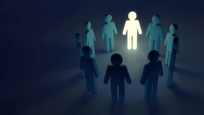 A circle of stick figure people stand together. One is illuminated and appears much brighter than the rest.