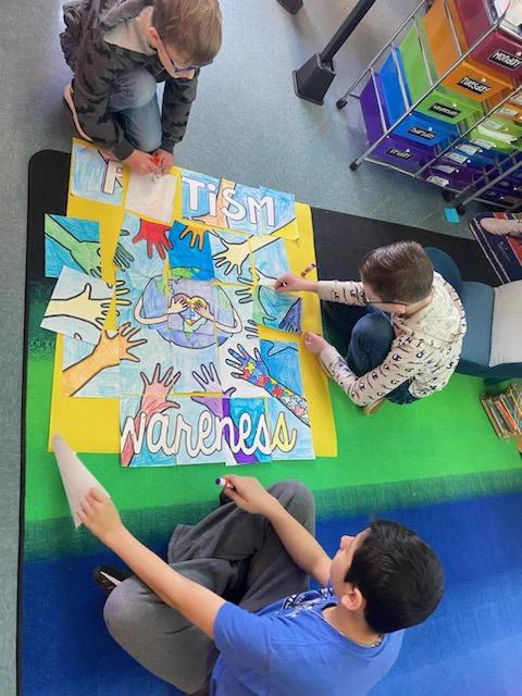 Three boys on the floor putting together an Autism Awareness poster.