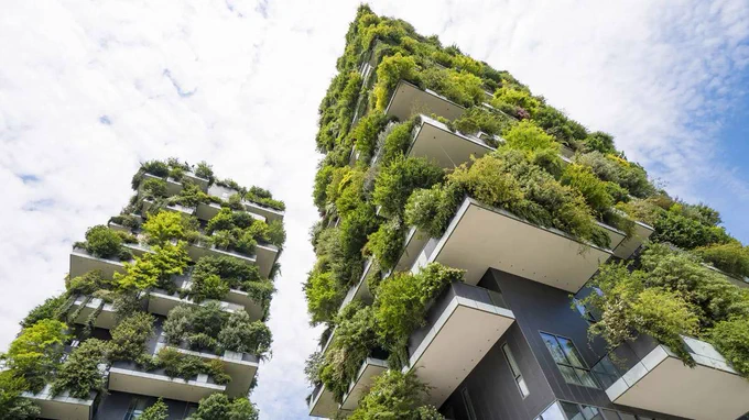 Two tall buildings covered in greenery against a blue sky. They have many balconies and look like nice places to live. 