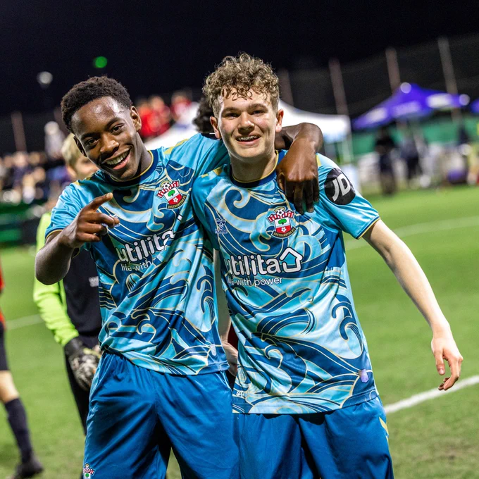 Two of Southampton's Under 16s players wearing the blue away kit smile and point to the camera in celebration after scoring at the Mina Cup in Dubai