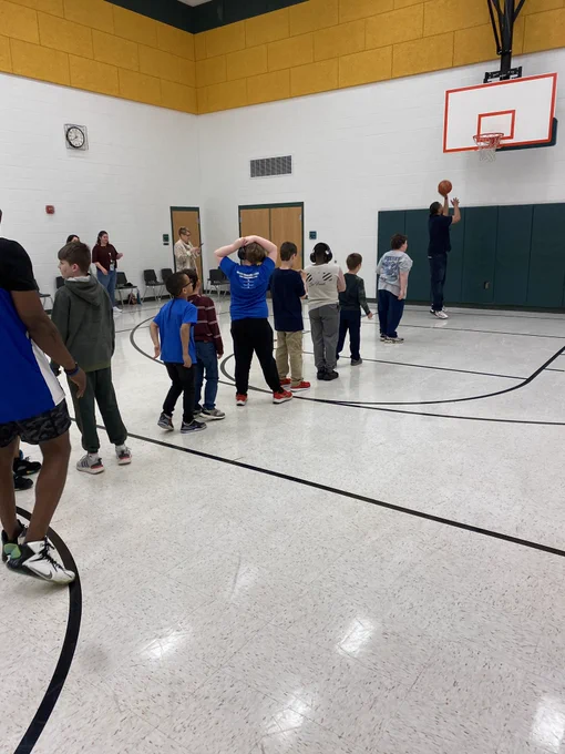 Elementary students taking basketball shots during game break.