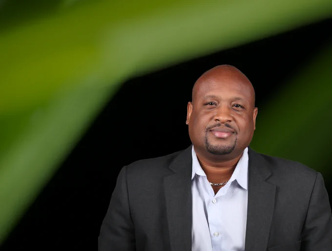 Corey Johnson, a bald black man in a gray blazer, sits against a black background with green stripes.