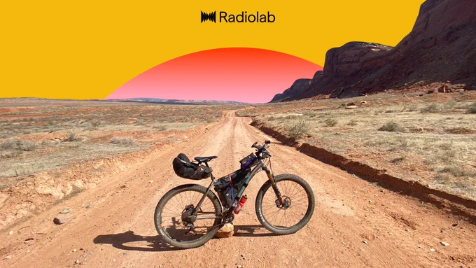On a dirt road, a bike packed to the brim sits against a desert backroung. The sky is yellow, and the Freq plays the role of a setting (or rising) sun. Art by Jared Bartman.