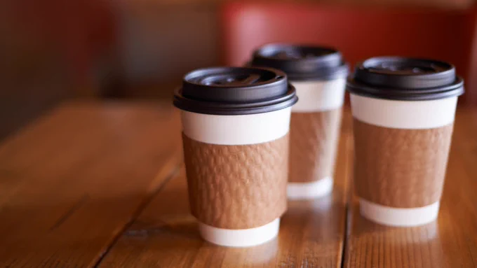 Image of three coffee cups with lids on a wooden table. 