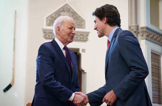 Prime Minister Justin Trudeau and President Joe Biden are standing in the Prime Minister’s West Block office. They are shaking hands and smiling.