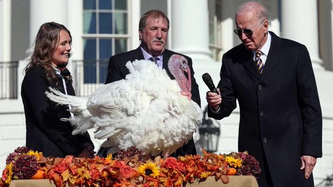 Joe Biden holding a microphone up to a turkey pardoned on Thanksgiving.