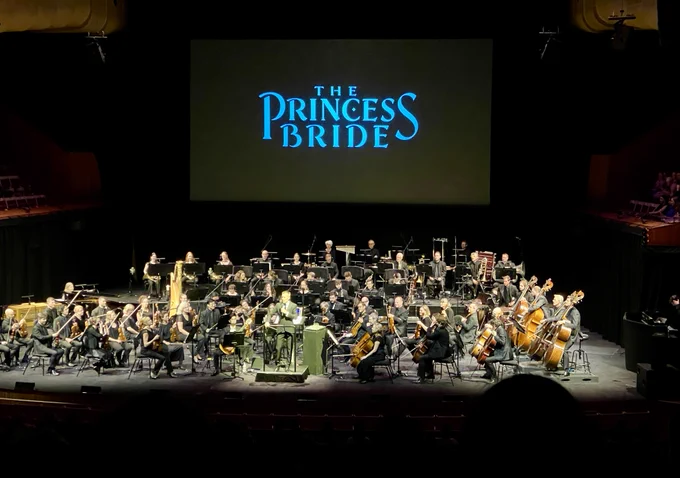 An orchestra sitting in front of a screen show 'the princess bride'.

