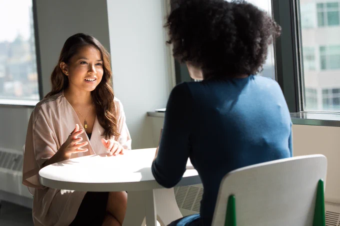 Deux femmes discutent assises à une table. 