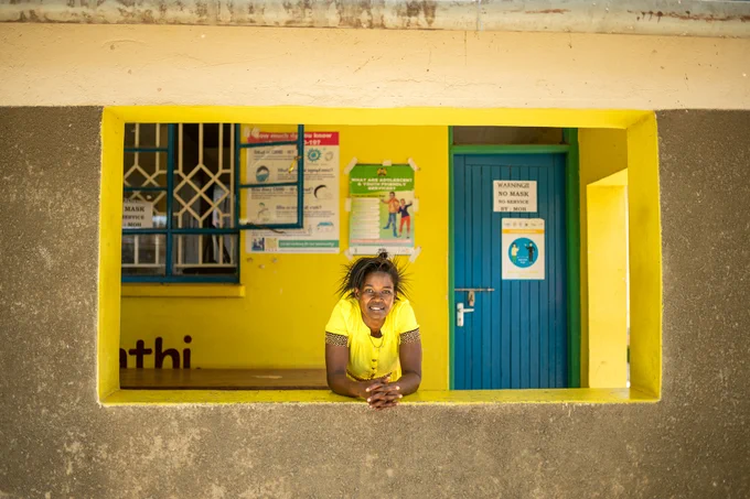 Woman wearing a yellow top leaning over counter smiling.