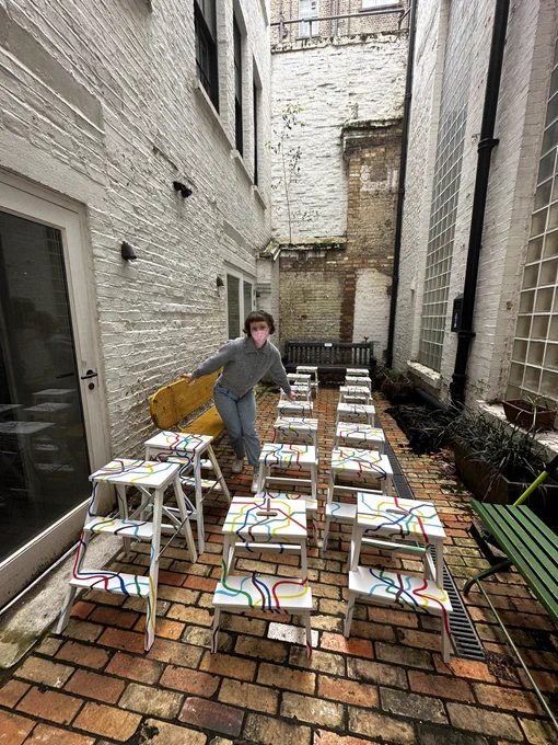 Set designer Alice Hallifax stands in a courtyard surrounded by stools and ladders with painted tube map patterns