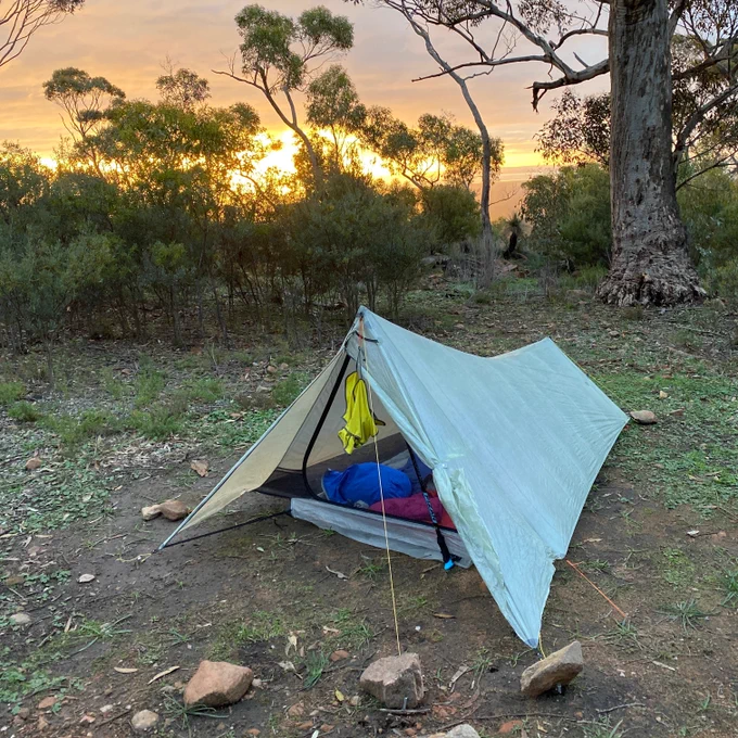 Tent at sunset, with orange sky behind eucalyptus trees