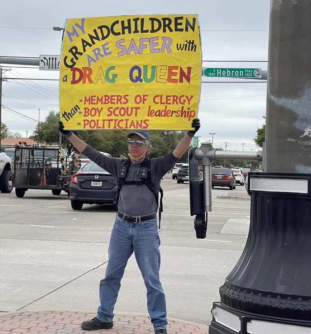 Picture of a man in Texas holding up a sign that says "My grandchildren are safer with a drag Queen than members of clergy, Boy Scout leadership, and politicians"