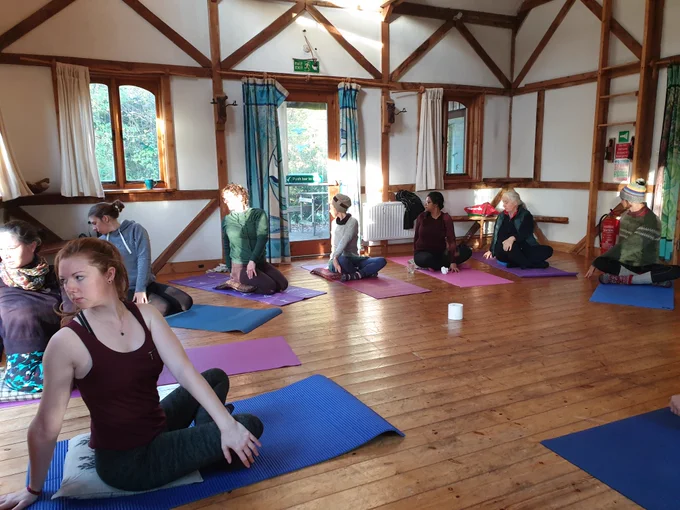 People doing a twisted yoga pose in a beautiful wooden building - the Oak House. Sunlight coming in through the windows.