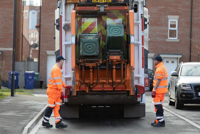 Bins being emptied into a refuse wagon, two men in orange high visibility clothing supervise