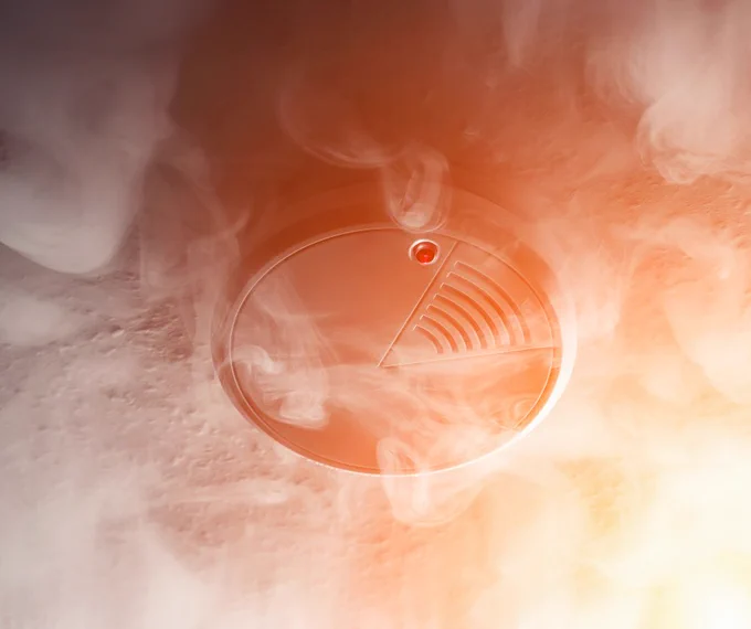 A smoke alarm fitted to a ceiling surrounded by smoke 