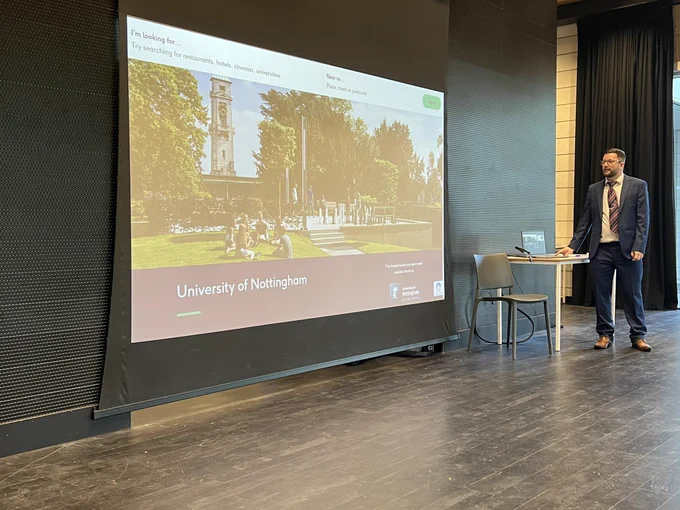 Dean from AccessAble demonstrating the AccessAble website. A screen behind him shows the website homepage for University of Nottingham