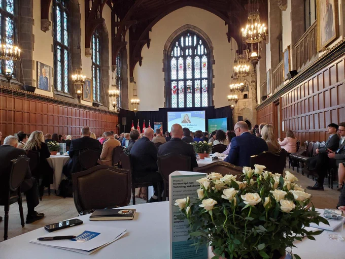 Attendees sit at tables and listen to a presentation 