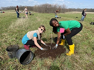 Young white girl and Black woman planting a tree at Kane County Forest Preserve District