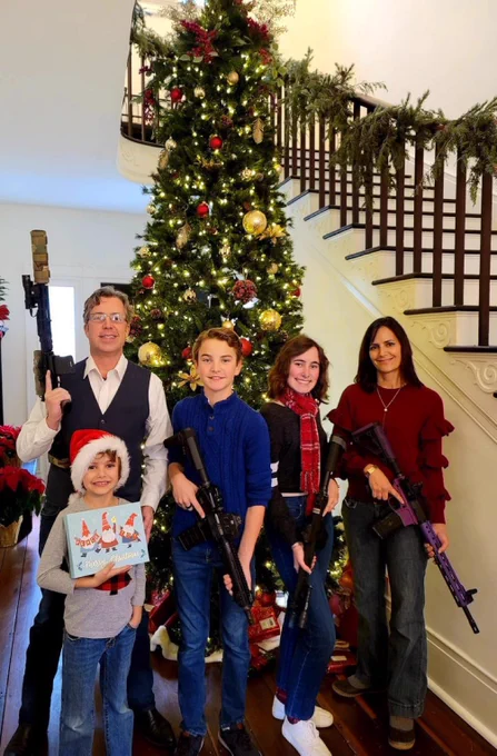 Congressman Andy Ogles posing with his family in front of a Christmas tree holding various assault rifles