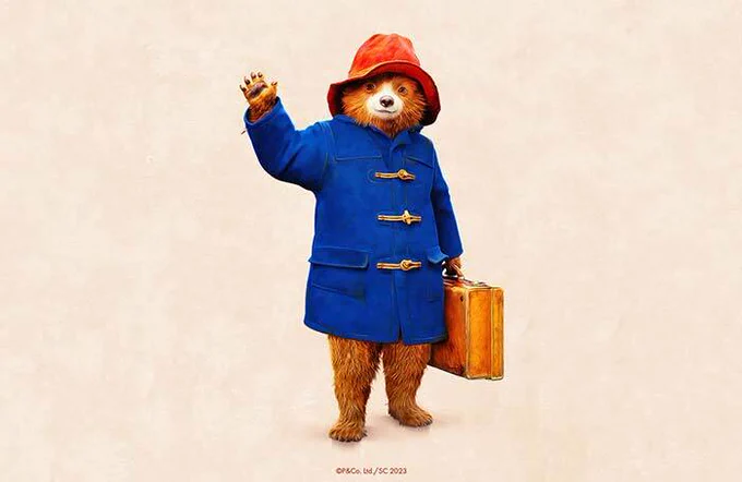 Paddington bear on his blue coat and red hat, waving