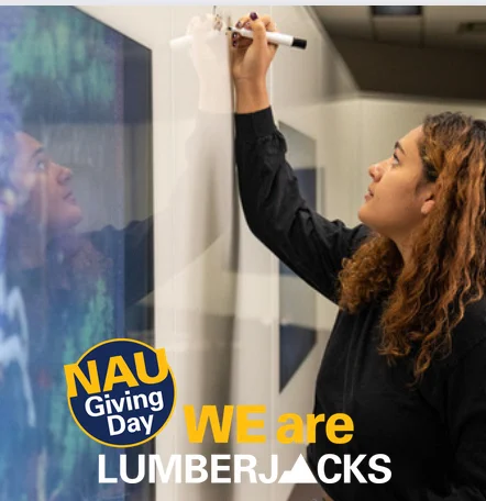 A young woman using a marker to write on a whiteboard wall.  She is looking up at what she is writing. At bottom: Logo for NAU Giving Day including phrase "WE are LUMBERJACKS".