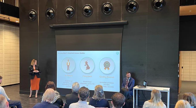 Anna Nelson presenting on AccessAble’s 23 year history to an audience at the University of Nottingham. On screen are highlighted points about AccessAbles surveying process focusing on in person assessments, consistency of information throughout the UK and a fully quality assured process.