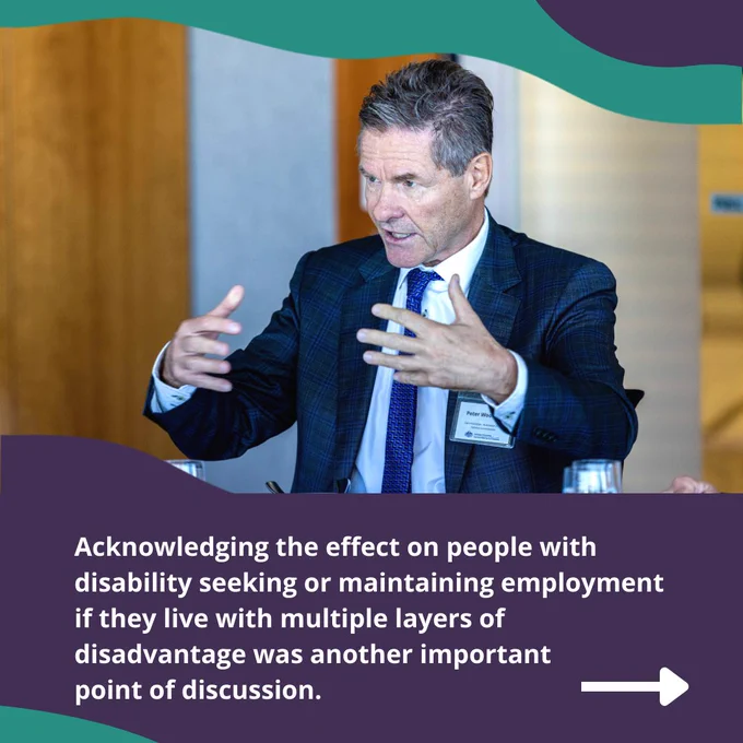 A man wearing a suit and tie is sitting in a room and talking to a group of people with his hands in front of him. Text: Acknowledging the effect on people with disability seeking or maintaining employment if they live with multiple layers of disadvantage was another important point of discussion 