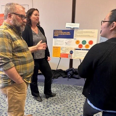 John Doherty and Theresa Carlson in front of their poster.  At right is an attendee who is listening to John, who is gesturing with one hand.