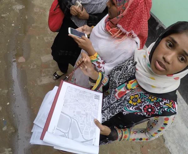 A woman in a street in Dhaka holding a printed out Field papers map. Photo from the Missing Maps Project.