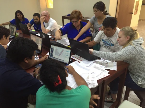 A bunch of people around a table digitizing Field Papers printouts into their laptops. Photo from a mapping party in Ecuador, by the Ecuadorian Red Cross.