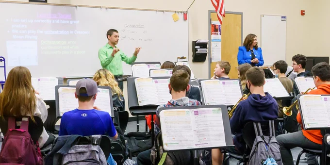 A band director conducts a group of middle school students in a school band room.