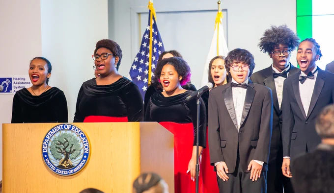 A group of students in tuxedos and formal dresses singing at the Department of Education.