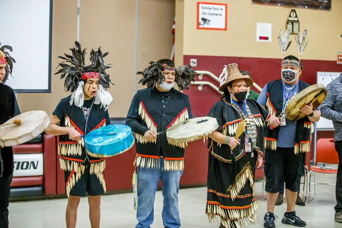 A group of Native American students performing in traditional dress with drums.