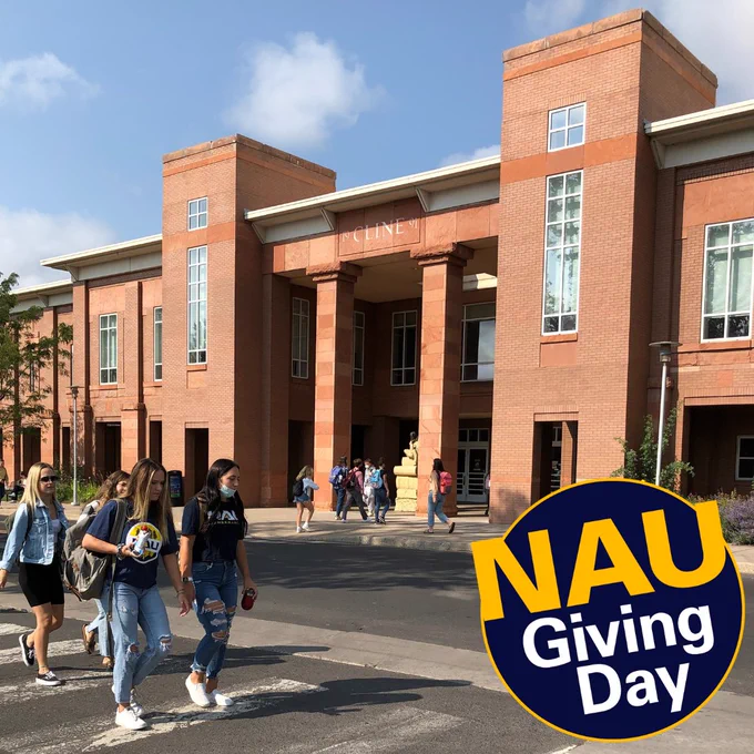 A view of the front entrance of Cline Library. There are students walking on the sidewalk in front of the library and, in the foreground, students walking across a crosswalk across the street form it.  It is a sunny day and there are clouds in the sky.  At bottom right: the NAU Giving Day logo.