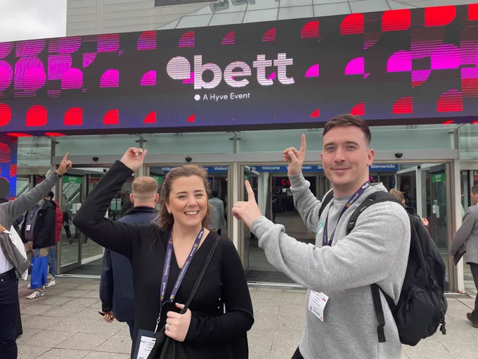 Cara Bielecki and Joe Dawber pointing at a sign that says "Bett: A Hyve Event".