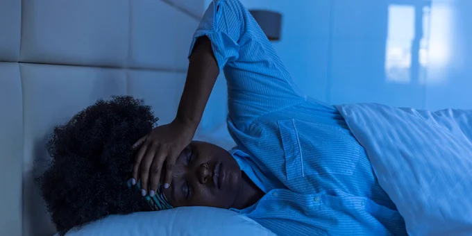 A woman lies in bed looking tired and stressed