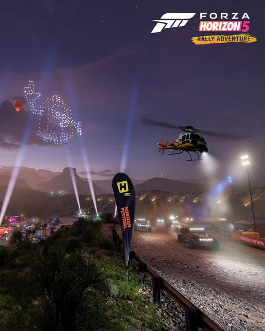 A rally race comes over a hill with a  helicopter above at night